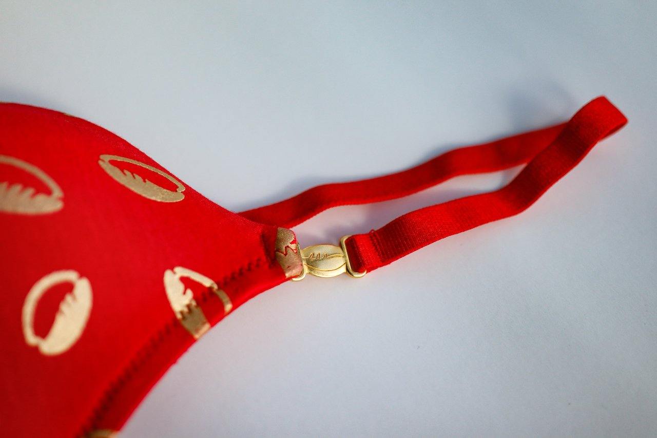 close up shot of red ebony and ivory yemaya bra showing gold cowrie shell bra strap clasp 
